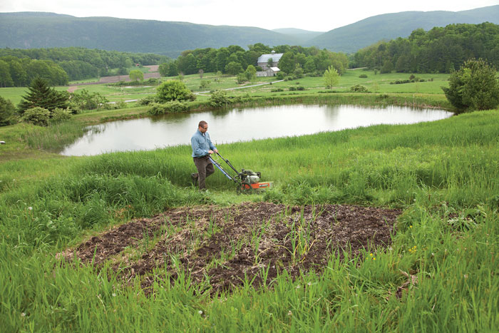 male using trimmer mower by pond