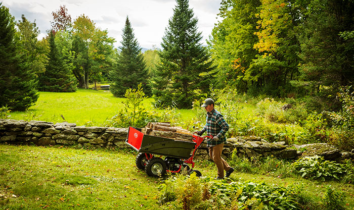 A man uses a power wagon to move a load of wood uphill.