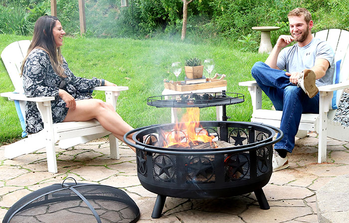A couple sits next to a fire pit, conversing.