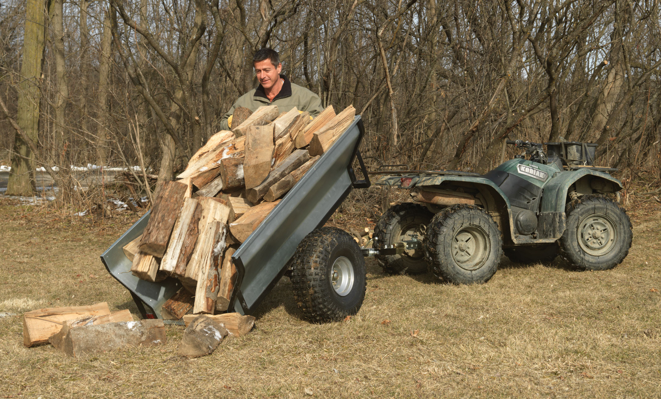 An ATV with a utility trailer being used to transport a load of firewood.