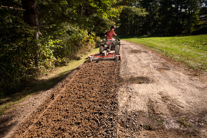 An ATV with a grader is used to fix pitholes in a driveway.