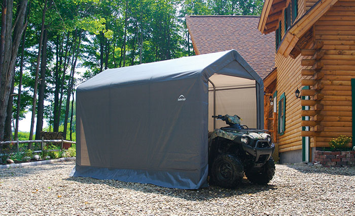 A Shed-in-a-Box® shelters an ATV in front of a log cabin home.