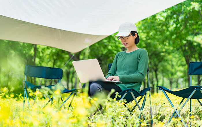 A woman works on a laptop under a portable shelter.