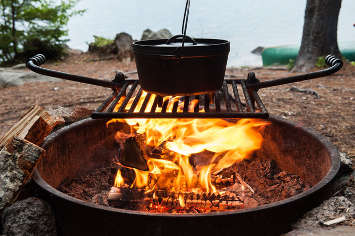 a fire ring sits next to a lake, a cast iron pot sitting on a grill rack above it.