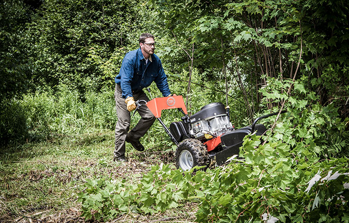 A man uses a field and brush mower to cut down thick brush and saplings