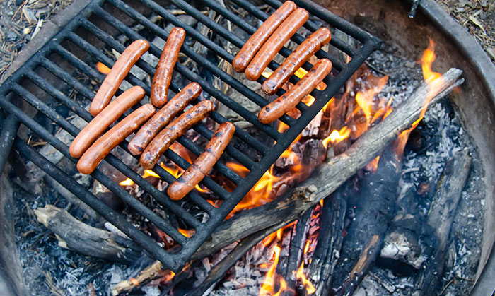 hot dogs cook on a grill