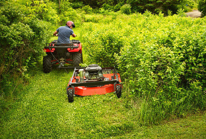 ATV with a rough-cut mower being used to mow tall overgrowth.