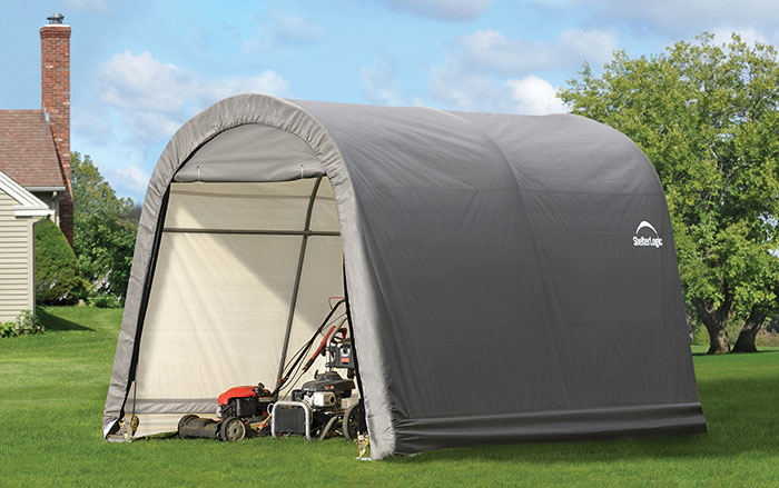 A portable shed stands in a backyard, lawn mowers and power equipment are stored inside it.