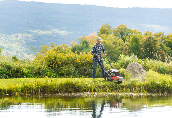 male using trimmer mower by pond